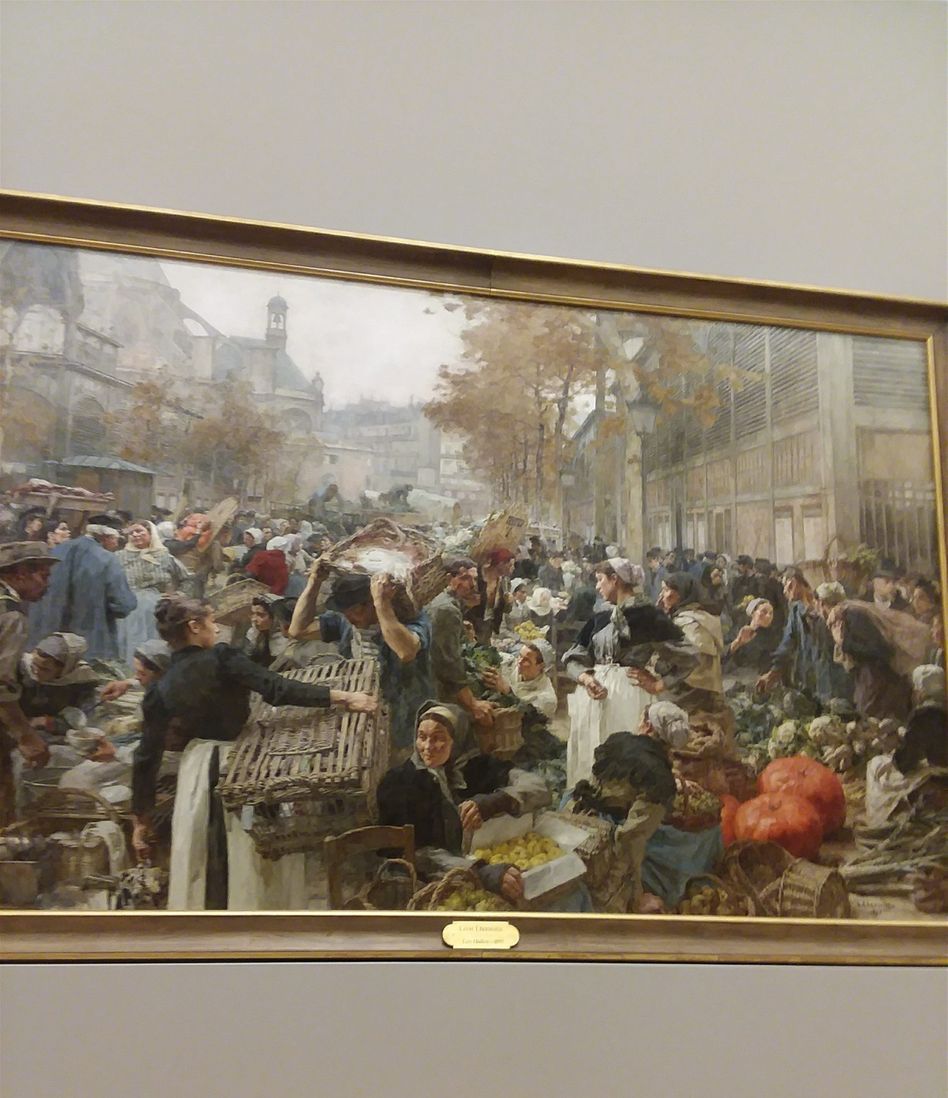 This is a photo of the Painting that León Lhermitte was commissioned to paint for Paris city hall around 1888. He chose Les Halles as the subject. This painting is now in the Petite Palais Museum. The artist depicted a delivery of products to a very crowded and lively market. The Seine River was a lively route for bringing merchandise into Paris. The landing at Les Halles was a major delivery point for meat products,vegetables, and all sorts of other food items. Les Halles shopping center and Place Joachim-du-Belly are just the opposite character of this scene now. Les Halles shopping center is really modern and beautiful. None of the buildings depicted around the original Les Halles in this painting exist today.